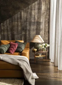 A cozy living room featuring a brown leather sofa with green and red throw pillows, a wooden side table with a ceramic lamp a