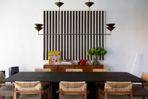 A minimalist dining room with a black table and woven chairs.