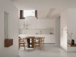 Modern minimalist residential kitchen featuring white wooden cabinets, a circular dining table with wooden chairs, and a larg