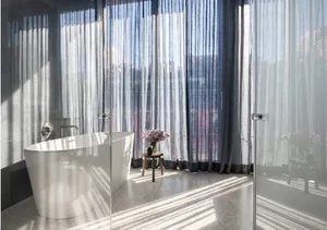 A modern bathroom with a white ceramic freestanding bathtub and sheer curtains allowing natural light in.