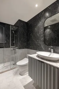 A modern residential bathroom with marble tiles, metal accents, and a white toilet.