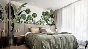 A bedroom featuring a modern bed with green bedding and a wall adorned with plant leaves.