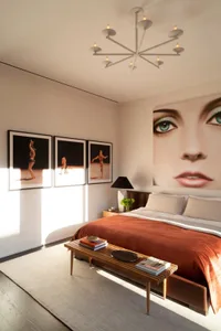 A modern bedroom with a bed covered in a tan textile, framed artwork, and a chandelier with candles.