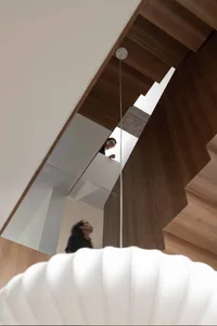 A modern interior space featuring a wooden staircase with a white sphere-shaped light fixture in the foreground.