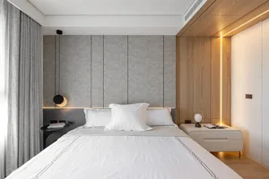 Modern minimalist bedroom featuring a white bed against a textured wall with soft lighting and wooden accents.