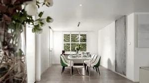 A modern minimalist dining space featuring a white marble table and white chairs with green accents.