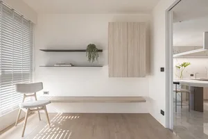 A minimalist living room with a light wood floor, white walls, a floating cabinet, and a plant.