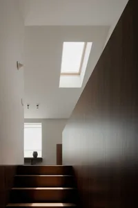 Minimalist modern staircase illuminated by natural light through a skylight and a window.