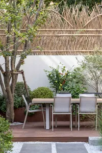 A modern wooden garden table with chairs surrounded by trees and plants.