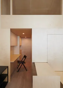 Modern minimalist kitchen with light wood cabinets and black chair.
