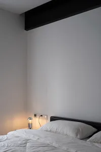 Minimalist bedroom with white pillows on an unmade bed, featuring a single light bulb on a bedside table.