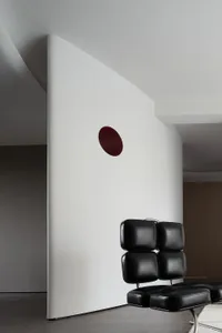 A minimalist interior space featuring a black leather cushion and a red circular feature on the wall.