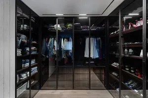 Modern closet with wooden shelves and glass doors displaying neatly arranged clothing and shoes.