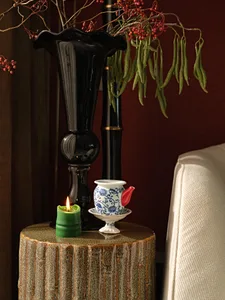 A ceramic teapot with red spout, blue floral pattern, and white base and saucer, placed on a textured wooden table with a gre