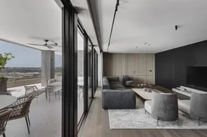Living room with grey sofa, armchairs, and coffee table, large floor-to-ceiling windows, and balcony with outdoor seating and