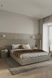 A minimalist bedroom with a fabric upholstered bed, white walls, and a large window with light-colored curtains.