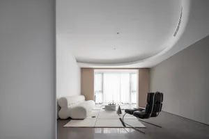A minimalist living room with a fabric sofa, leather chairs, and a glass coffee table.