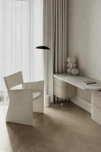 A minimalist residential interior featuring marble and concrete materials, with a modern chair, a desk with a lamp, and a war
