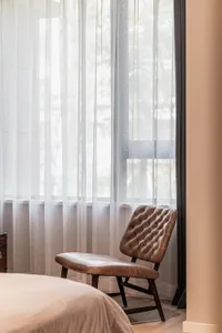 A modern bedroom featuring a leather upholstered chaise lounge under transparent curtains.