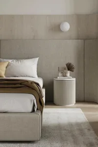 A modern minimalist bedroom with a fabric bed, wooden headboard, and a sleek, rounded bedside table with a marble top.