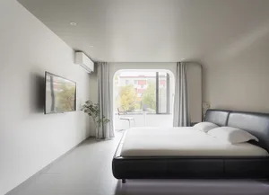 A modern bedroom featuring a white fabric bed, minimalistic decor, and a large window with a view of trees and buildings.