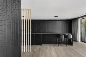 A stylish, minimalist kitchen featuring black cabinets, wooden flooring, and a sleek bar counter.