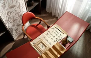 A modern home office with a red leather desk and chair, featuring calligraphy and a traditional vase.