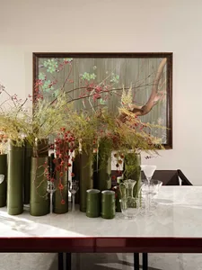 A modern interior setting featuring a table adorned with ceramic vases and glasses, with a large framed artwork in the backgr