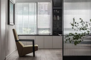 A modern living room featuring a comfortable chair, closed blinds, and a bookshelf with books and decorative items.