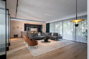 A modern living room with a grey sectional sofa, brown armchairs, and a round coffee table in a spacious room with large wind