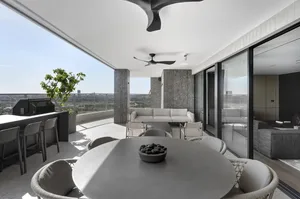 Modern living space with concrete walls, large windows, and a dining area with round table and chairs.