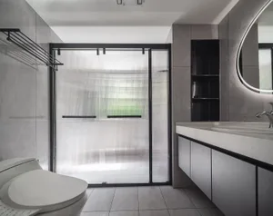 Modern minimalist bathroom with a glass shower door, white toilet, and dark grey tiles.