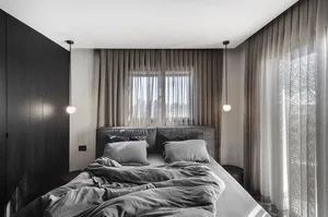 A modern minimalist bedroom with a textured bed, neatly arranged pillows, and sheer curtains.