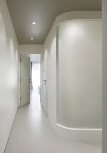A modern minimalist hallway with smooth, white walls and floors, featuring a glass wall and a concrete curve.