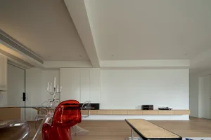 Modern minimalist living room with transparent red and glass furniture, wooden flooring, and white walls.