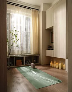 A minimalist home workout room with a green yoga mat, wooden floor, and white cabinets.