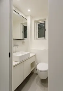 Modern minimalist bathroom with white tiles, a sink, and a toilet.