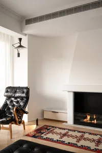 A modern living room with a white fireplace, leather chair, and patterned carpet.