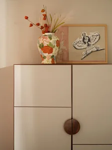 A minimalist cabinet with a neutral tone featuring a floral-patterned vase with dried flowers and grasses, and a framed artwo