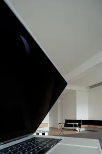 A minimalist home office setup featuring a sleek, modern desk and chair in a well-lit, white room with wooden flooring.