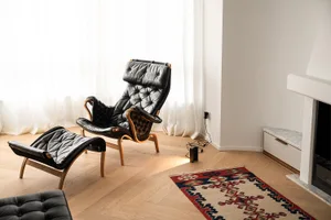 Minimalist living room featuring a leather chair, ottoman, and rug on a wooden floor.