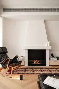A minimalist living room with a fireplace, hardwood floors, a black leather chair, and a patterned rug.