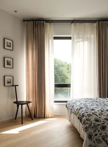 A minimalist bedroom featuring linen curtains, wooden furniture, and glass windows.
