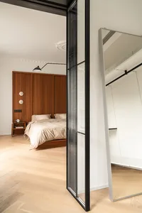 Modern minimalist bedroom featuring wooden walls, a glass closet, and a bed with neutral bedding.