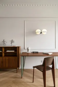 Minimalist home office featuring a wooden desk and chair against a white wall, with decorative items and lighting.