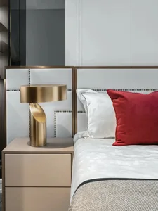 A modern bedroom with a white leather headboard adorned with gold accents and a red decorative pillow, featuring an arc lamp 
