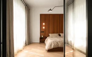 A modern bedroom featuring a wooden headboard, neatly made bed and soft fabric curtains allowing sunlight to filter through, 