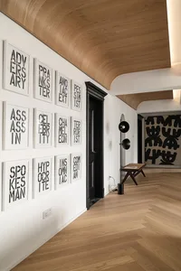 A modern corridor featuring hardwood flooring, framed text, and a black door.