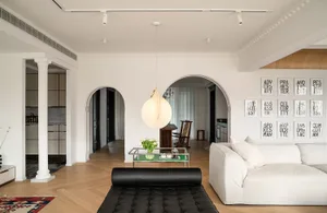 Modern minimalist living room with white walls and wooden flooring, showcasing a white sofa and black leather ottoman.