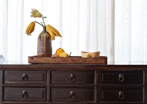 A wooden tray with a ceramic vase and fabric-covered items on a wooden dresser.